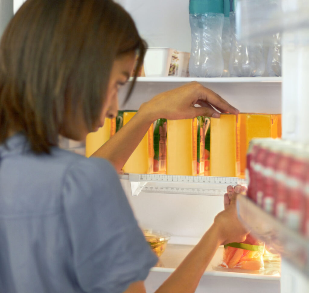 A woman arranges slices of cheese in a refrigerator. Other food items, including bottles and containers, are visible on the fridge shelves.